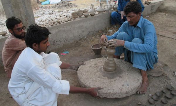 Description: A potter structuring a pot with the help of others. — Photo by Hanif Samoon