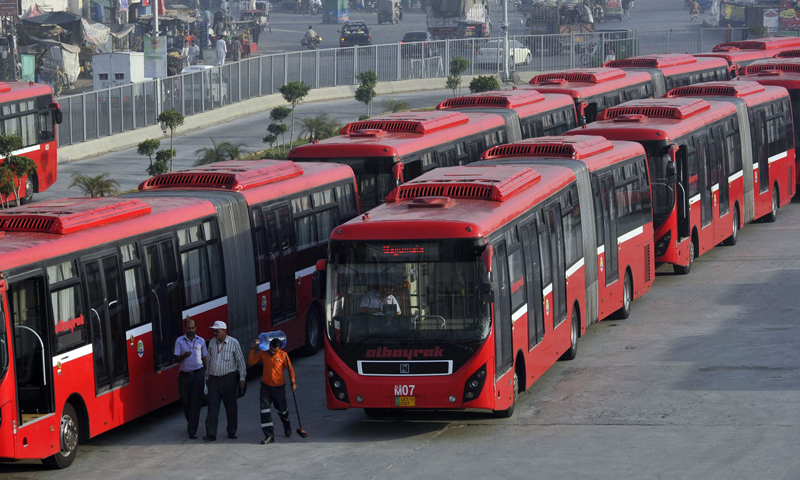 Description: This photograph taken on June 5, 2013, shows employees walking beside metro buses parked at a terminal in Lahore. — AFP Photo